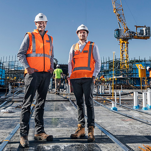 Directors Mathew and Daniel Edwards of Stephen Edwards Constructions, at a work site, in high viz, crane in background