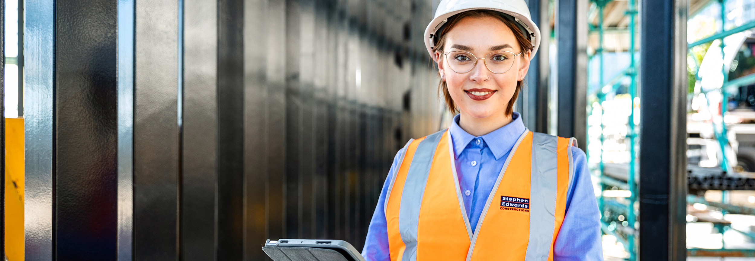 A female construction worker on site, high viz, checking standards